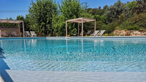 En pool med klart vatten, solstolar och en pergola.