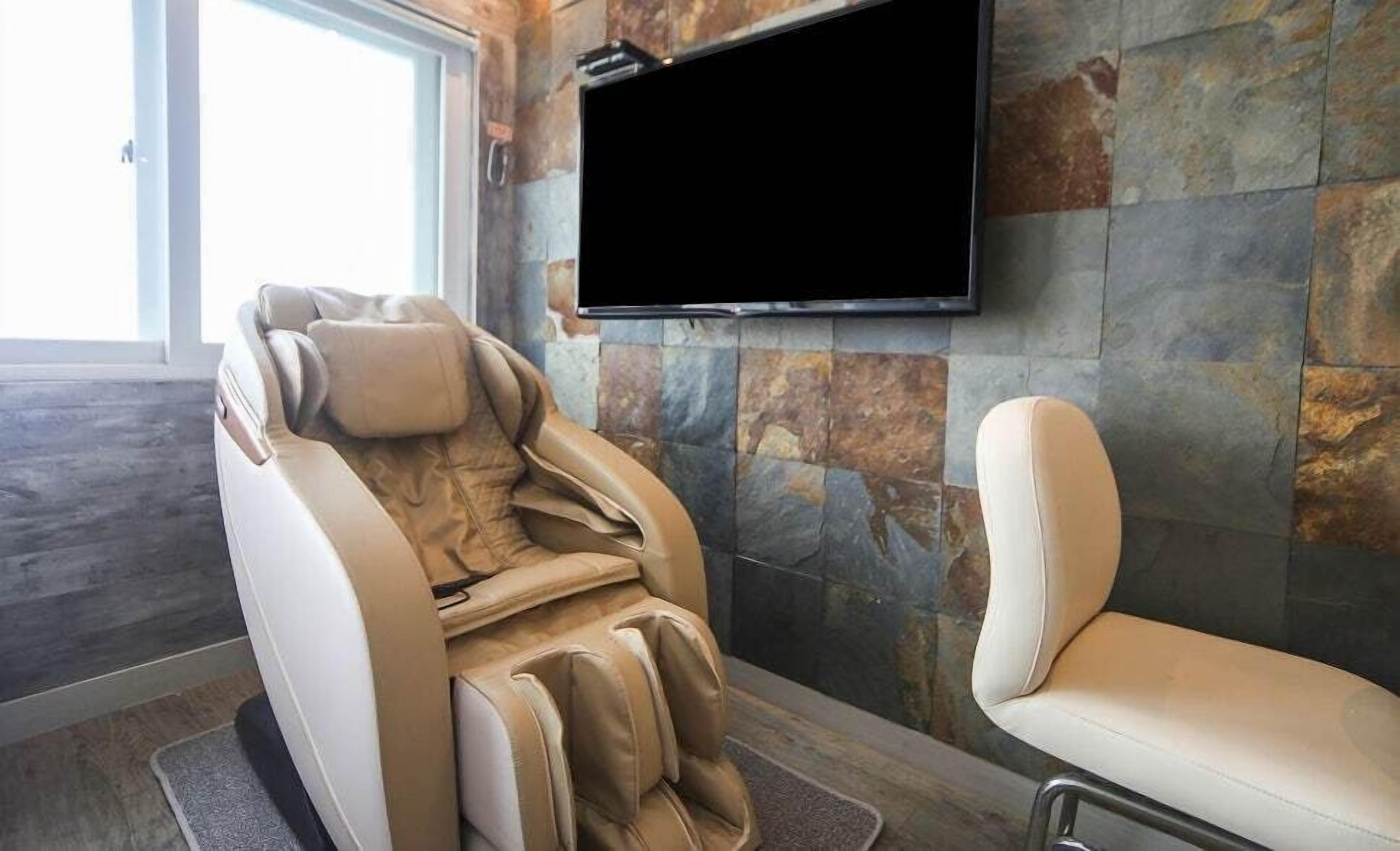 A massage chair in a room with stone walls and a flat-screen TV mounted on the wall.