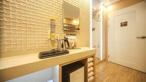 Une chambre d’hôtel avec un mur carrelé, un lavabo avec une bouilloire, un sèche-cheveux et une armoire où sont suspendus des vêtements.