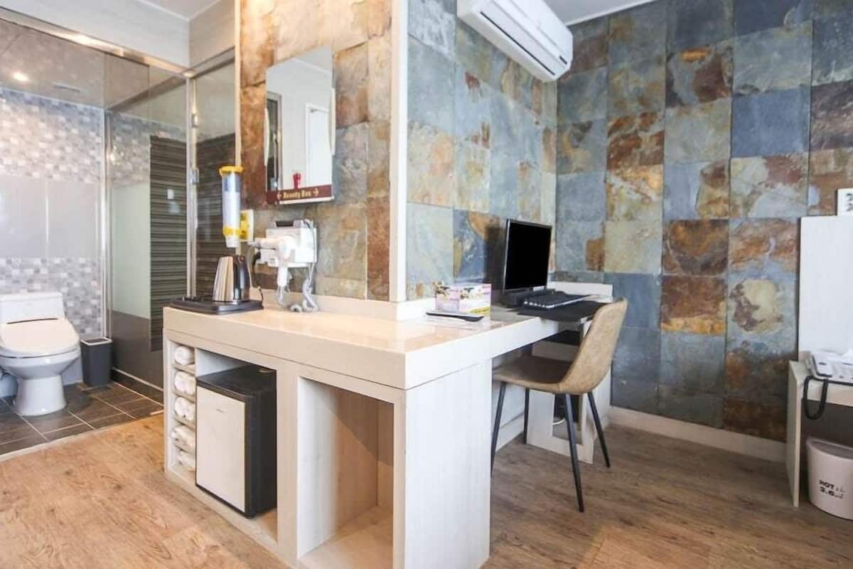 A modern bathroom with a shower, toilet, and a small desk with a chair.