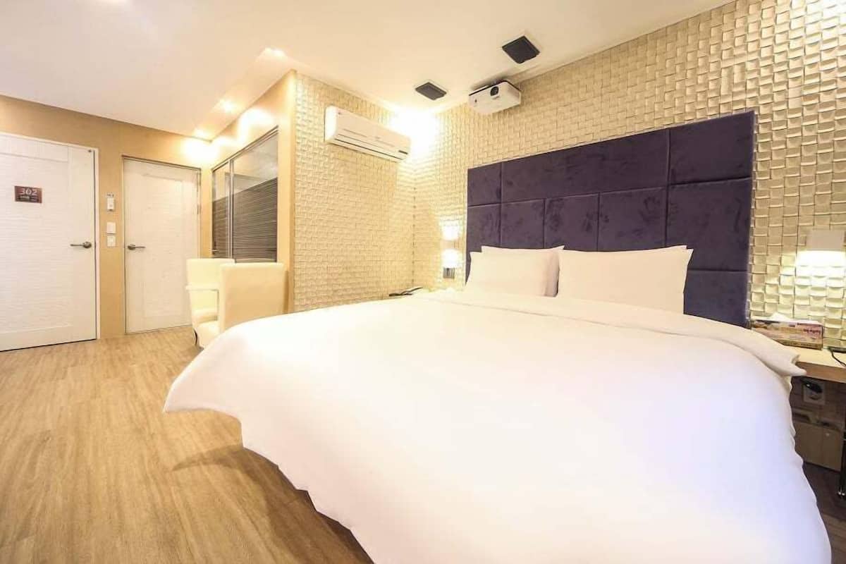 A hotel room with a large bed, a headboard, a mirror, and a wall-mounted air conditioning unit.