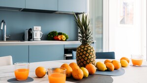 Keittiössä on ananas, appelsiineja ja lasillinen appelsiinimehua työtasolla.