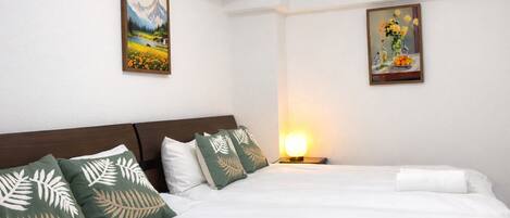 A hotel room with a large bed, two pillows, a nightstand with a lamp, and two framed pictures on the wall.