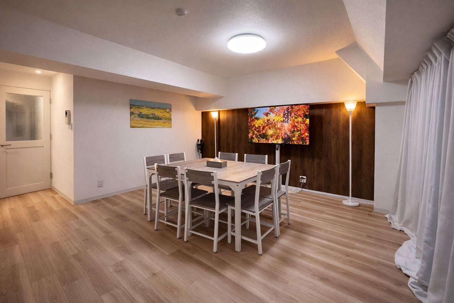 Un espace repas moderne avec une table et des chaises en bois, un tableau au mur et un grand écran de télévision.