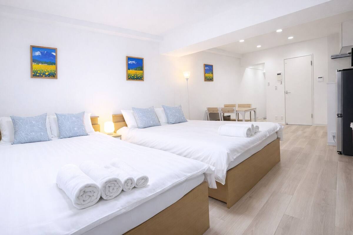 A hotel room with two beds, a desk, chairs, and artwork on the walls.
