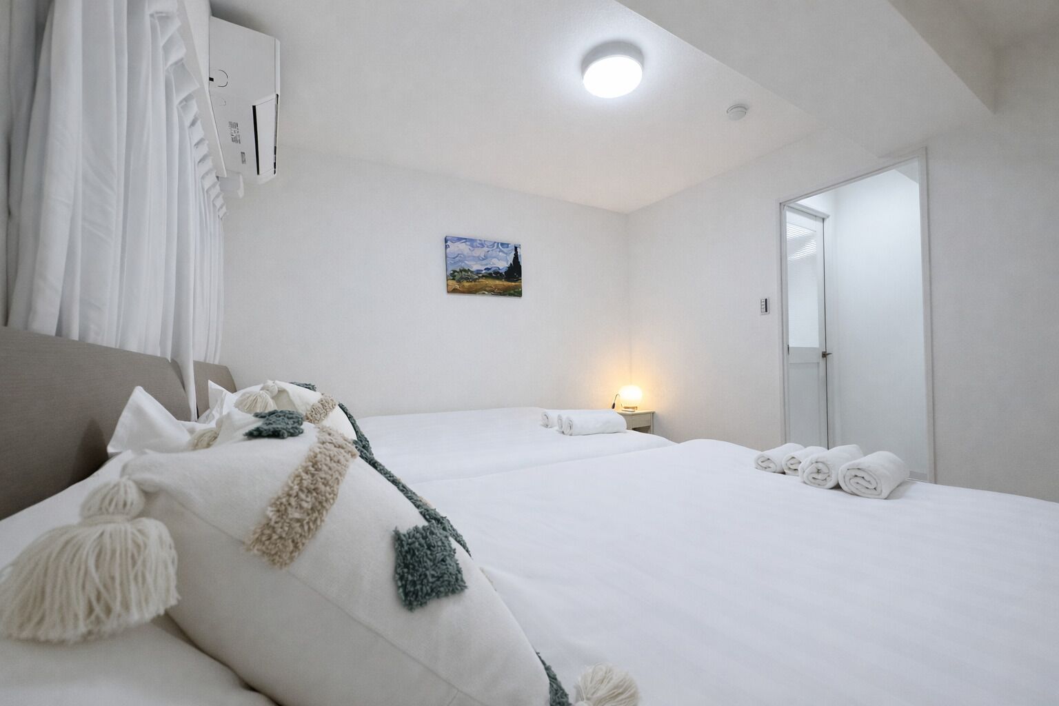 A hotel room with a large bed, a bedside table with a lamp, a painting on the wall, and a door.