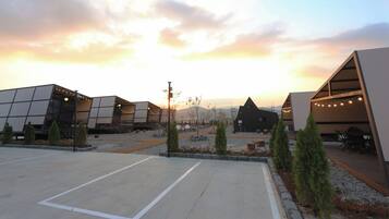 A modern building complex with multiple structures, including a large open area with a paved surface and a seating area with string lights.