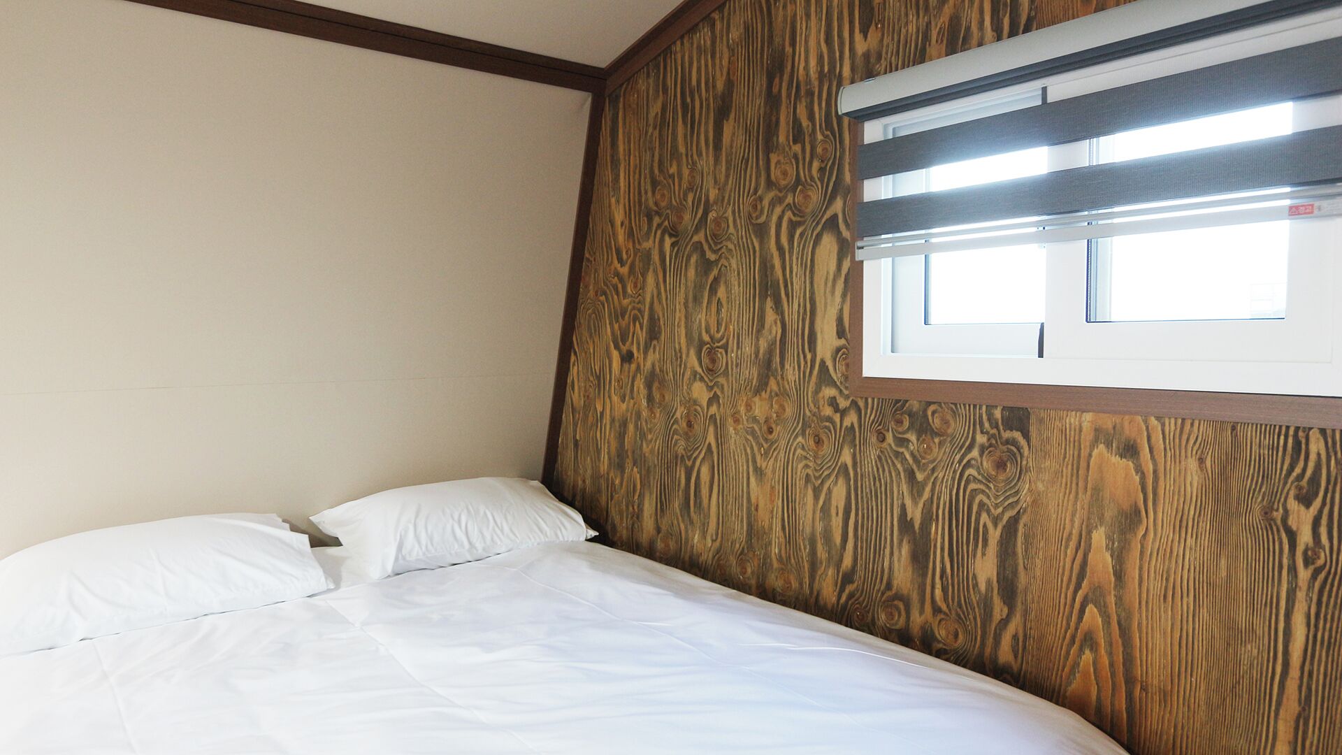 A bedroom with a wooden headboard, a single bed with white bedding, and a window with blinds.