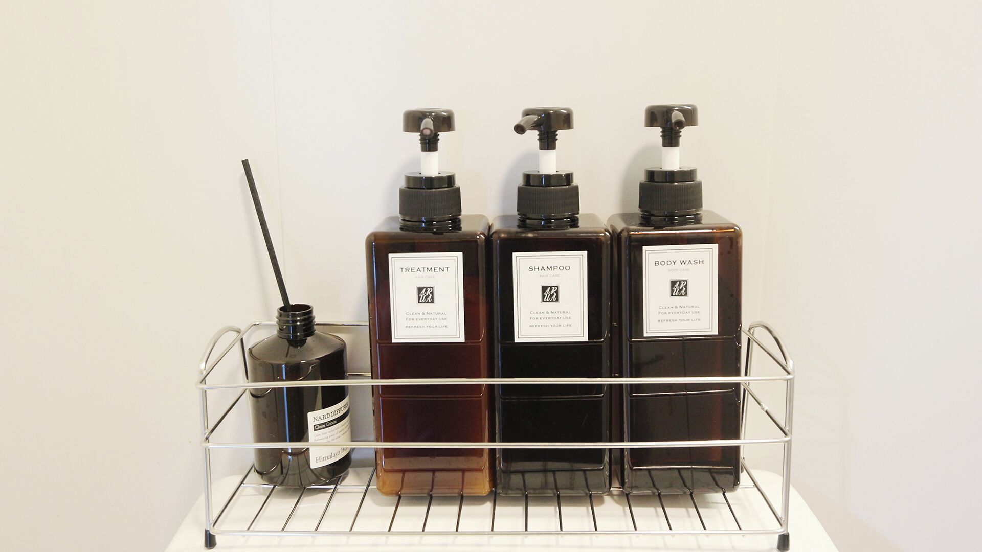 Une étagère en métal sur laquelle sont posées quatre bouteilles de produits pour les soins capillaires et un diffuseur.