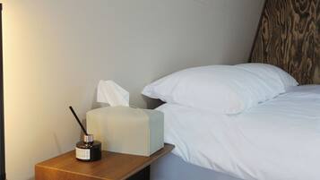 A neatly made bed with white linens, a bedside table with a tissue box and a black object, and a lamp on the left.