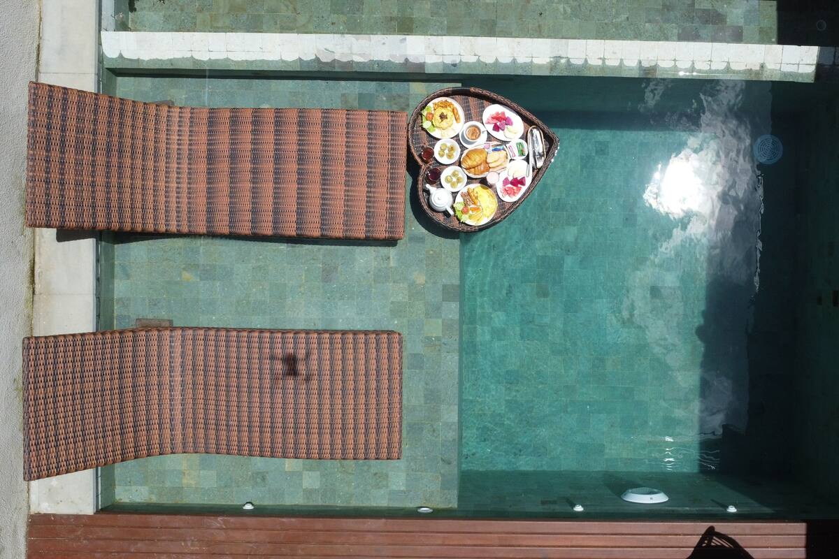 Luftaufnahme eines Schwimmbeckens mit zwei Liegestühlen und einem Tisch mit Speisen.