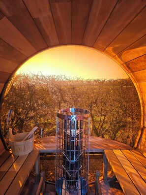 Une structure circulaire en bois, avec une cage en métal au centre, un banc en bois et une table en bois sur laquelle se trouvent un seau blanc et une cuillère.