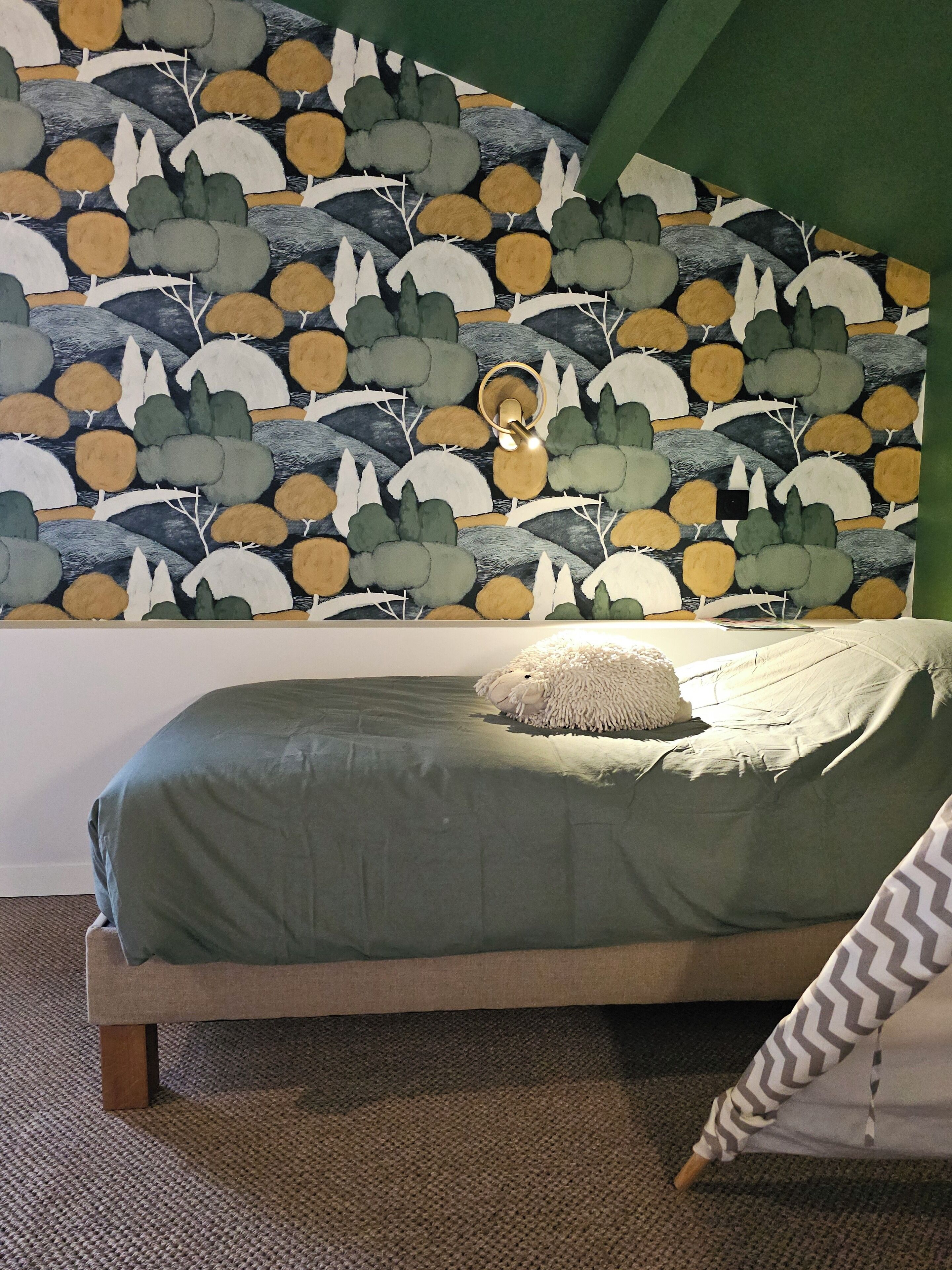 A bedroom with a bed, a green wall, and a patterned wallpaper.