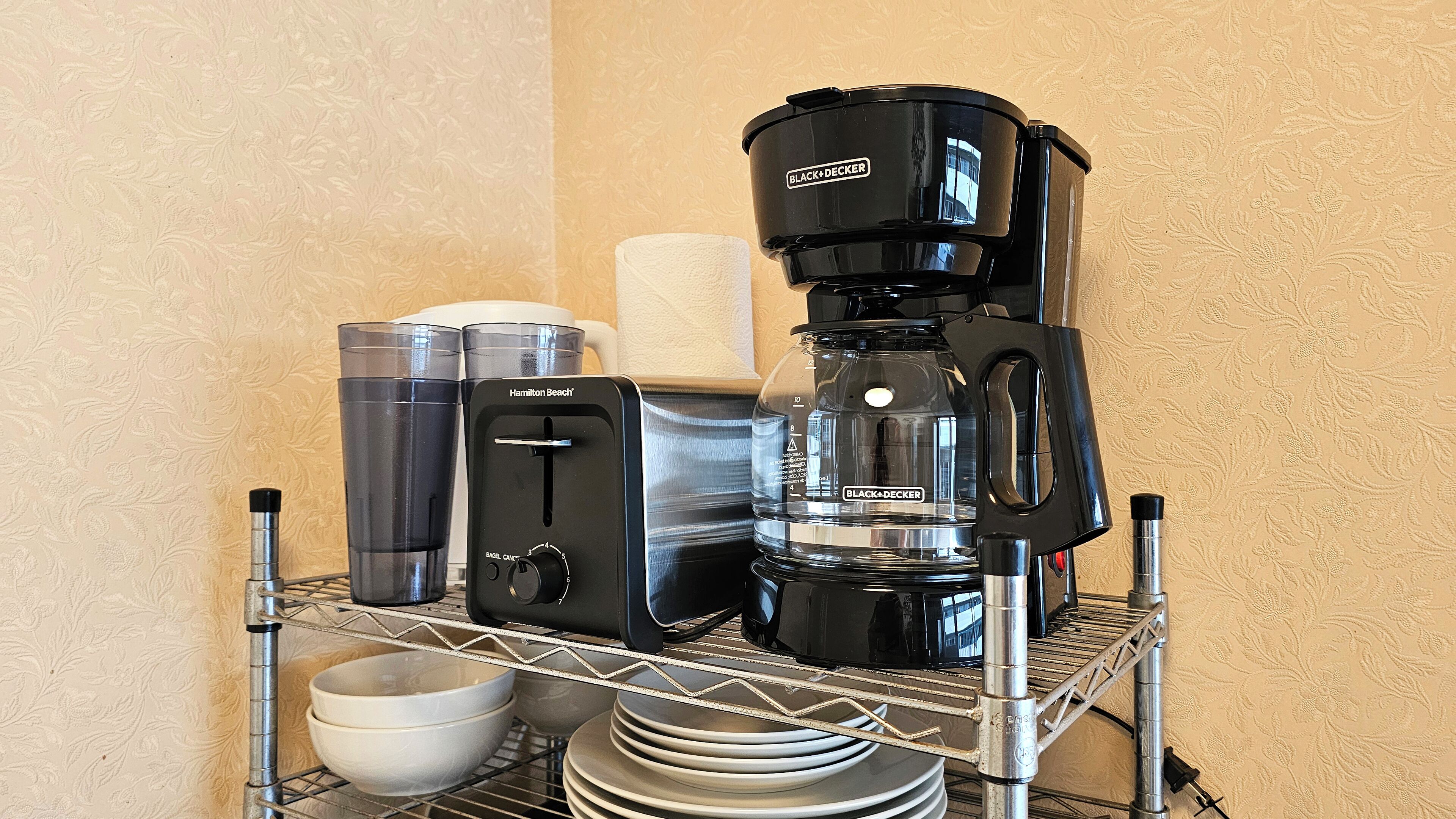 Un coin cuisine équipé d’une machine à café, d’un distributeur d’eau et d’un distributeur d’essuie-tout, le tout placé sur une étagère en métal.