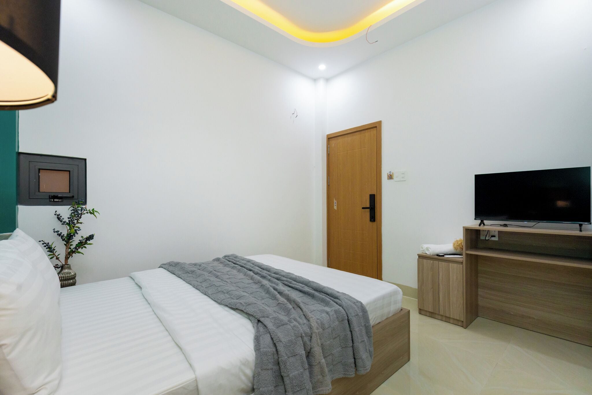 A bedroom with a bed, a television, a wooden door, and a small cabinet.