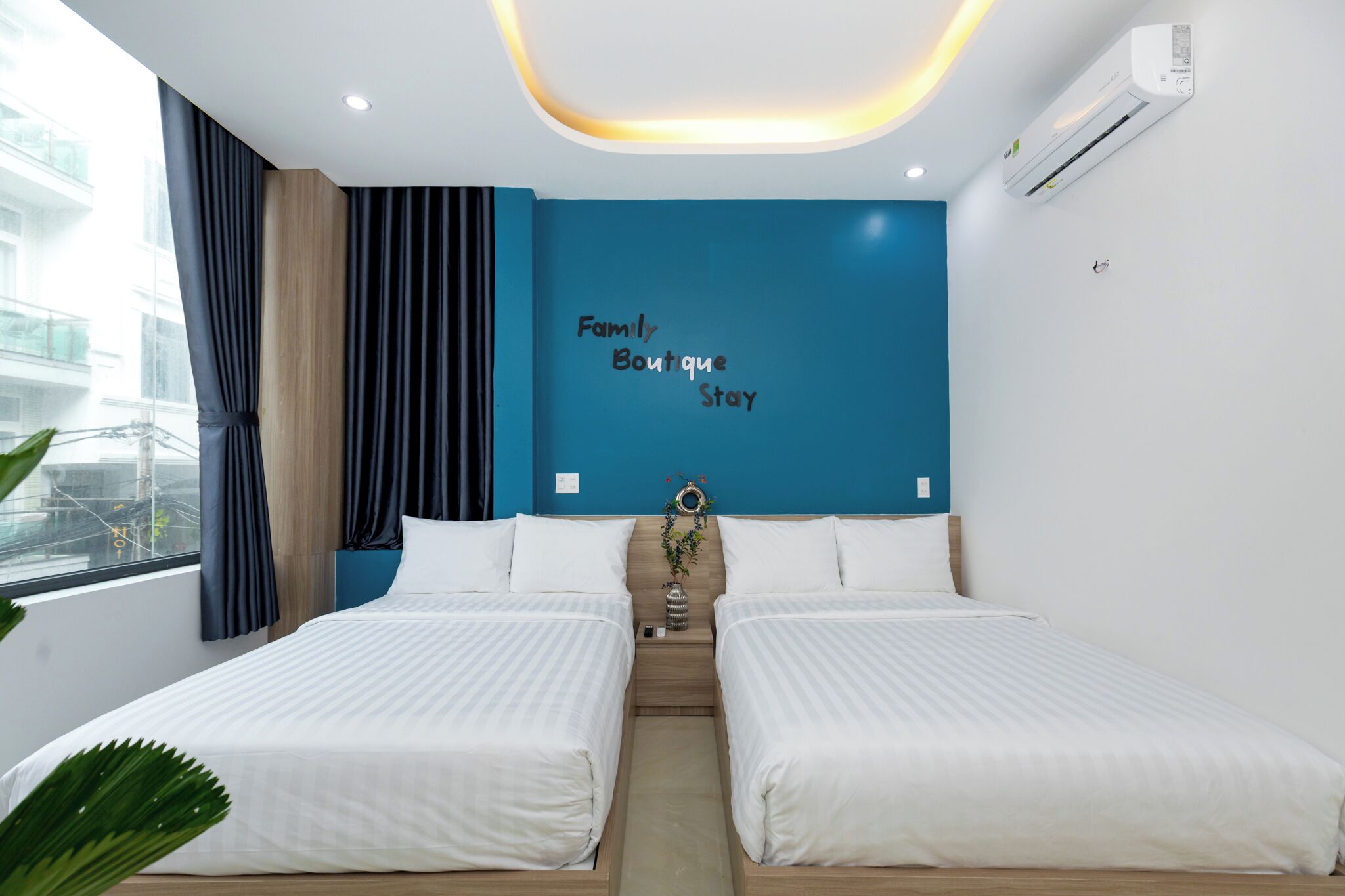 Quarto de hotel com duas camas, uma parede azul decorativa e uma janela com cortinas.