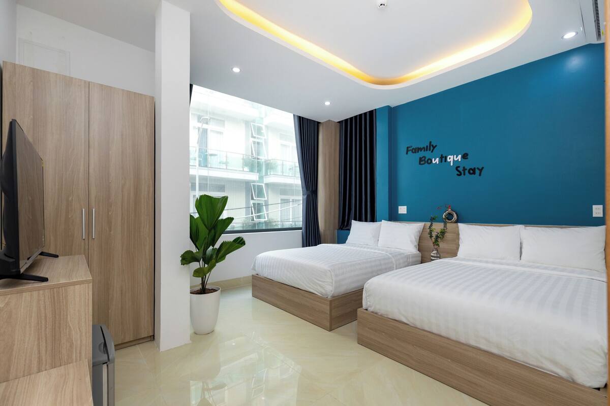A hotel room with two beds, a TV, a potted plant, and a view of the building outside.