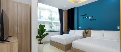 A hotel room with two beds, a TV, a potted plant, and a view of the building outside.
