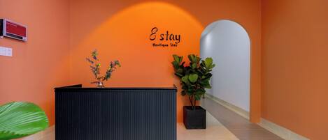 A reception area with a black reception desk, a potted plant, and a wall with the text "E stay Boutique Stay".