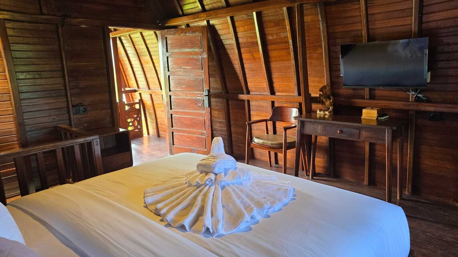 A hotel room with a large bed, wooden walls, a TV, and a desk with a chair.