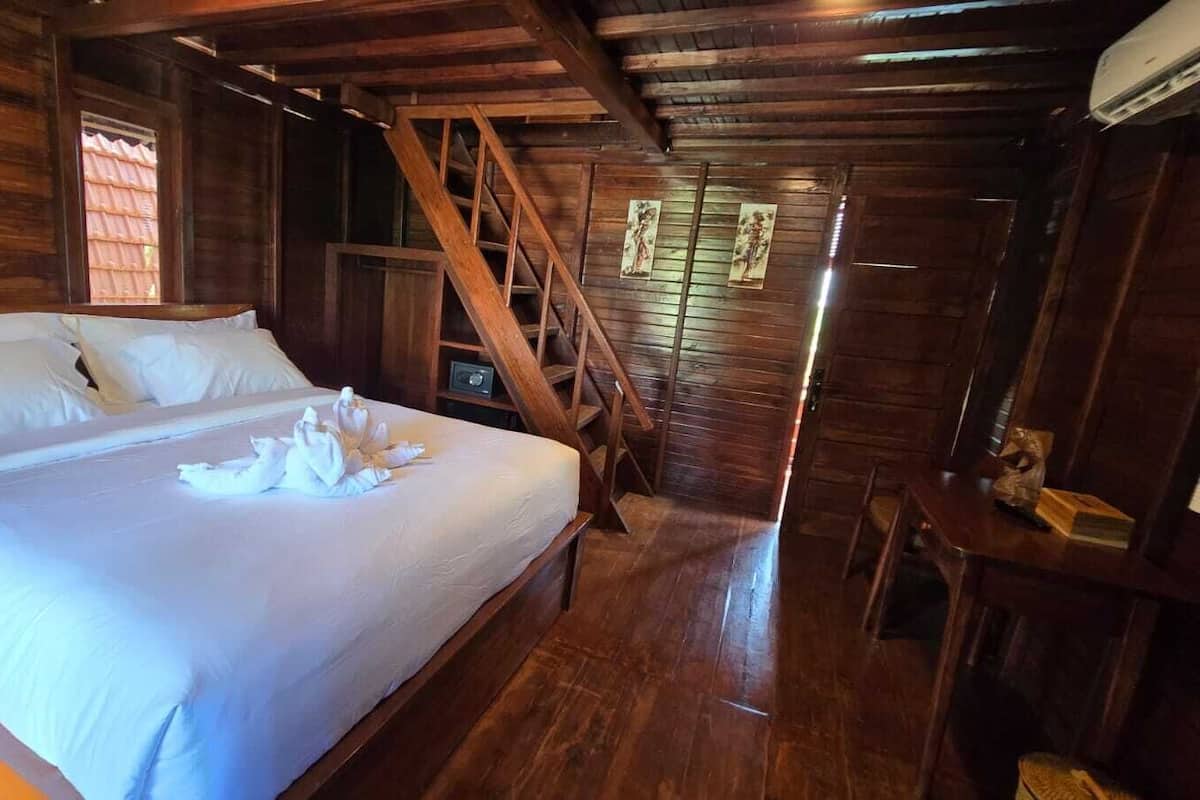 A wooden cabin room with a bed, a staircase, and a small table with a book.