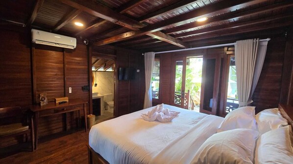 Ein holzgetäfeltes Zimmer im Chalet-Stil mit einem Bett, einem Schreibtisch und einem durch eine offene Tür erreichbaren Badezimmer.