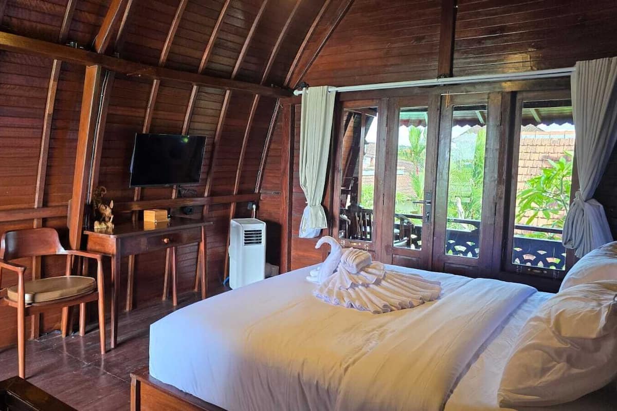 A wooden room with a bed, a desk, a chair, a television, and a window with curtains.
