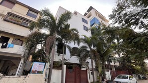 Un edificio residenziale con cancello automatico, un'auto bianca parcheggiata e diverse palme.
