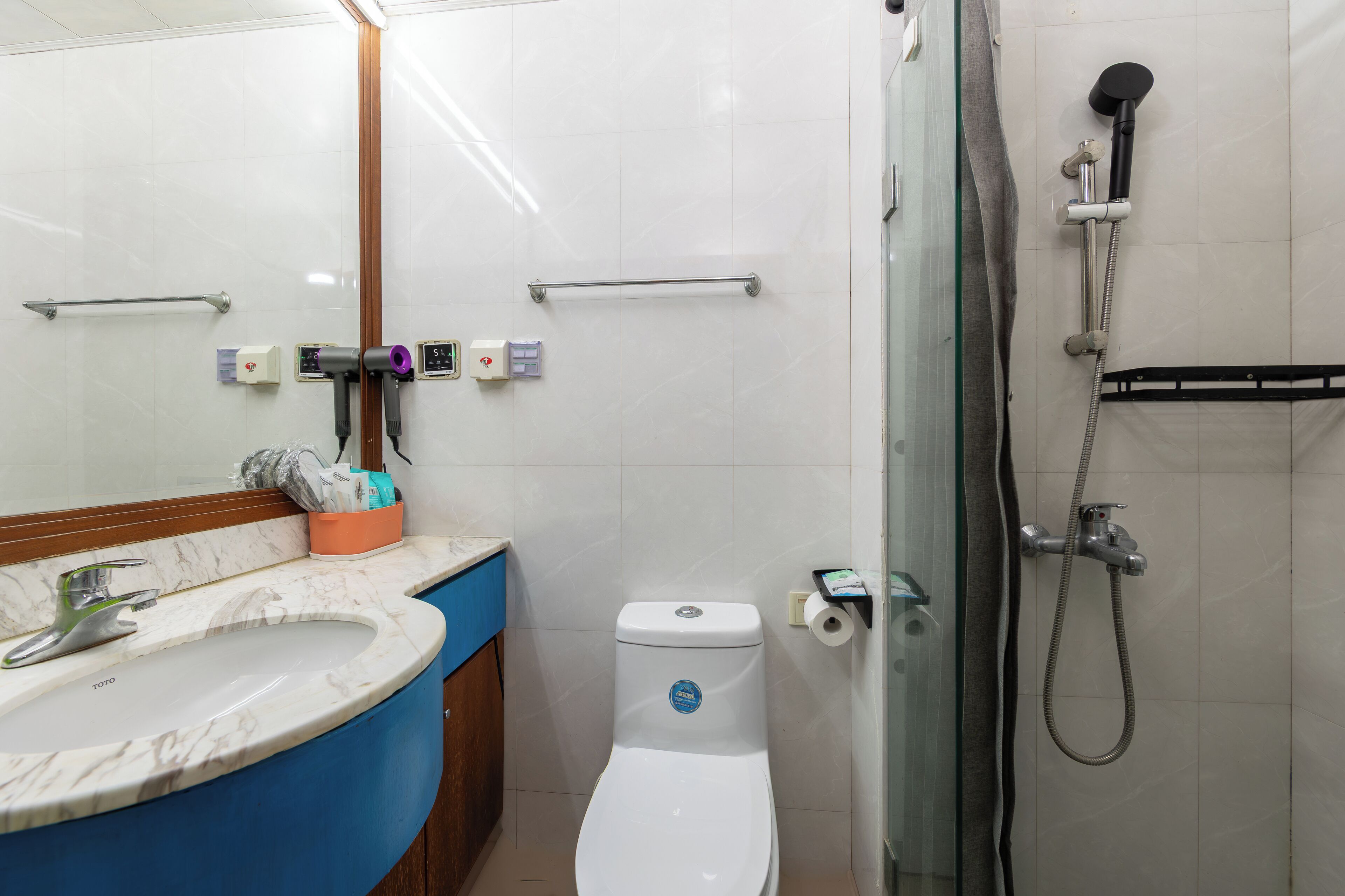 A bathroom with a white toilet, a sink with a marble countertop, a glass shower enclosure, and a towel rack.