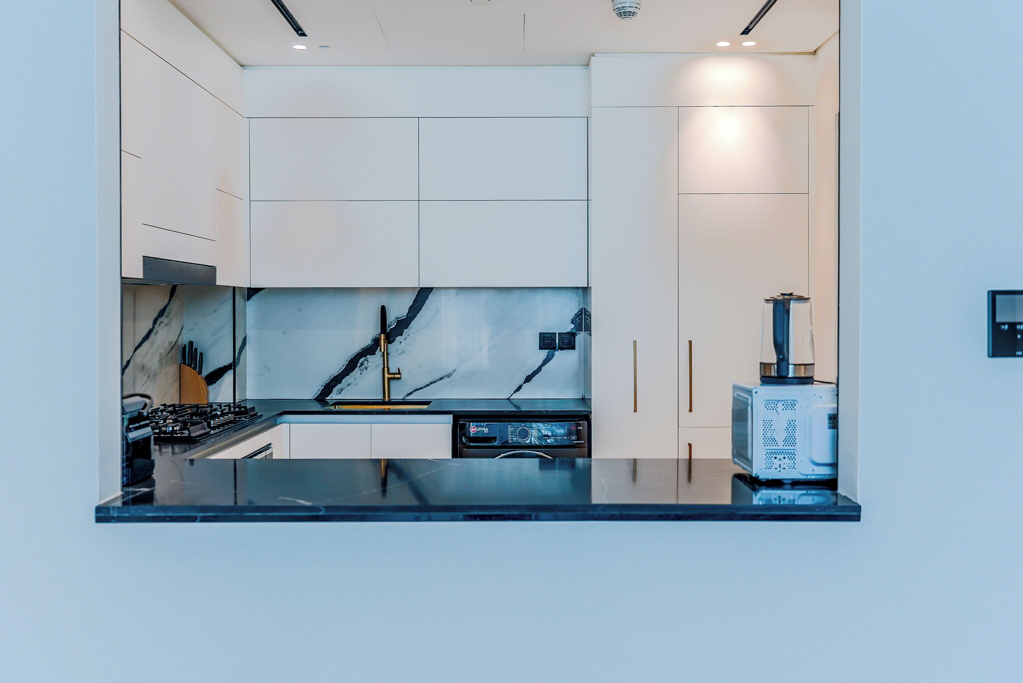 Une cuisine moderne avec des meubles blancs, un plan de travail noir et un pare-feu en marbre.