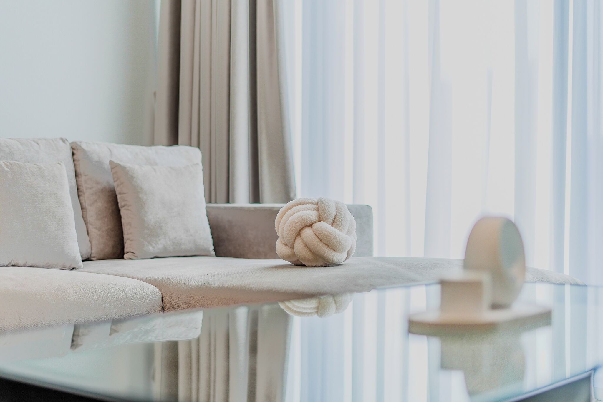 A modern living room with a sofa, a decorative knot pillow, and a glass coffee table.