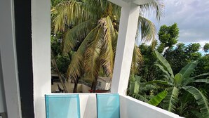 Un balcon avec deux chaises bleues, un mur blanc et une vue sur une végétation tropicale.