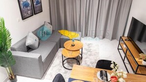 Una sala de estar moderna con un sofá gris, una mesa redonda de madera y un televisor sobre un mueble.