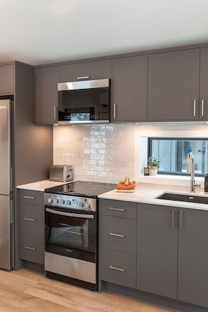 Eine moderne Küche mit grauen Schränken, einem Edelstahlkühlschrank, einem Einbauofen, einer Mikrowelle und einem Toaster.