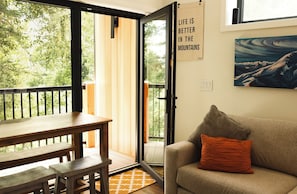 Ein Zimmer mit Holztisch und Bänken, einem Sofa mit orangefarbenem Kissen, einem Berg-Gemälde und einem Schild mit der Aufschrift 'LIFE IS BETTER IN THE MOUNTAINS'.