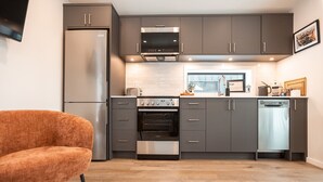 A modern kitchen with grey cabinets, a stainless steel refrigerator, an oven, and a dishwasher.