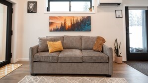 A living room with a grey sofa, two cushions, a painting above the sofa, and a potted plant.