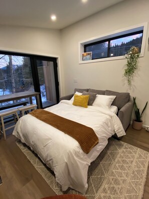 A bedroom with a large bed, a window with a view, a bench, and a potted plant.