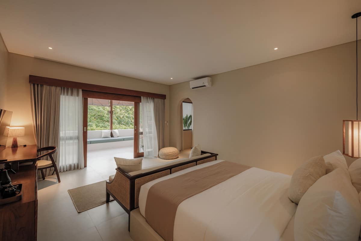 Une chambre d’hôtel équipée d’un lit, d’un bureau, d’une chaise, d’une fenêtre avec des rideaux et d’un appareil de climatisation.