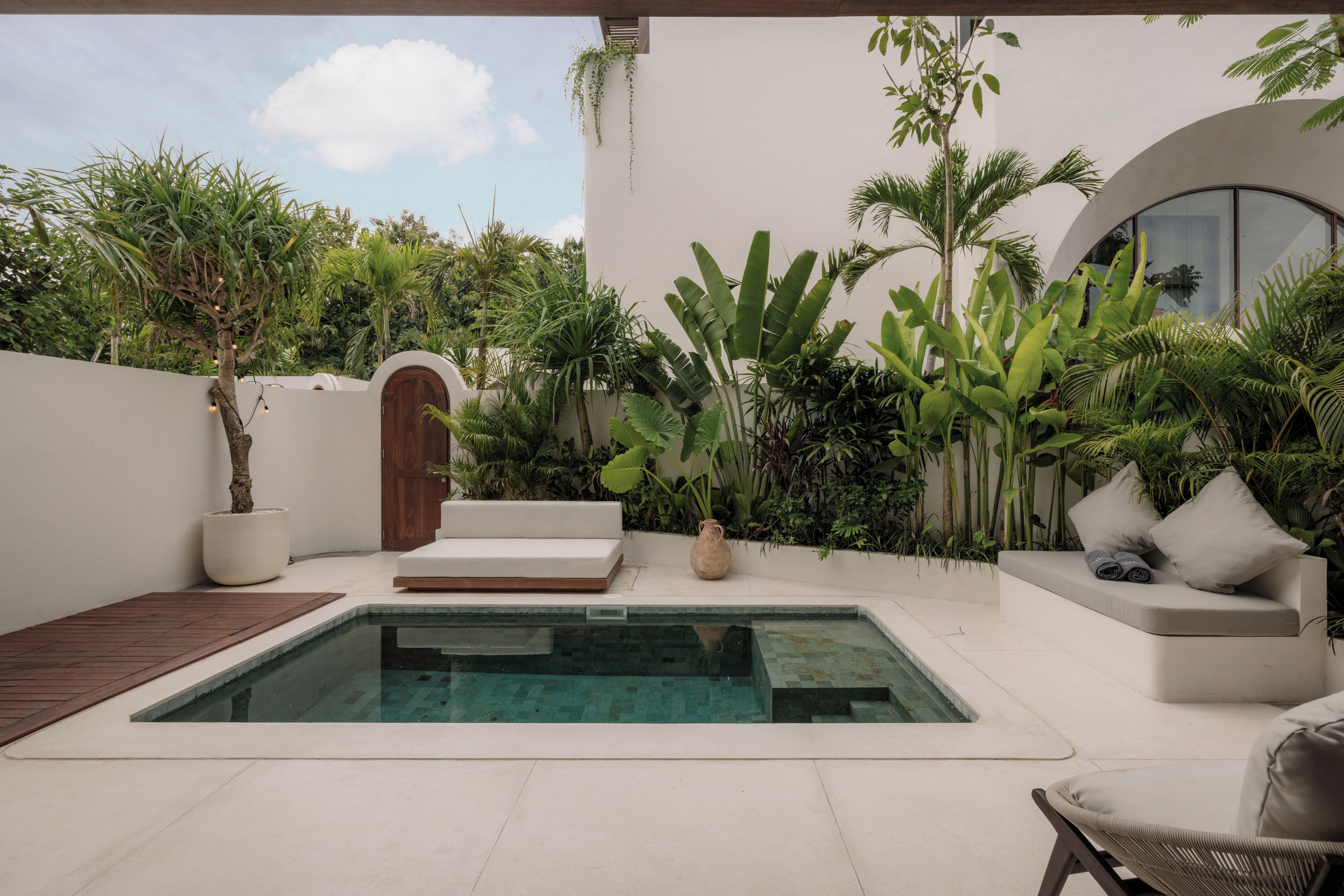 A modern outdoor pool area with a built-in seating area and lush tropical plants.