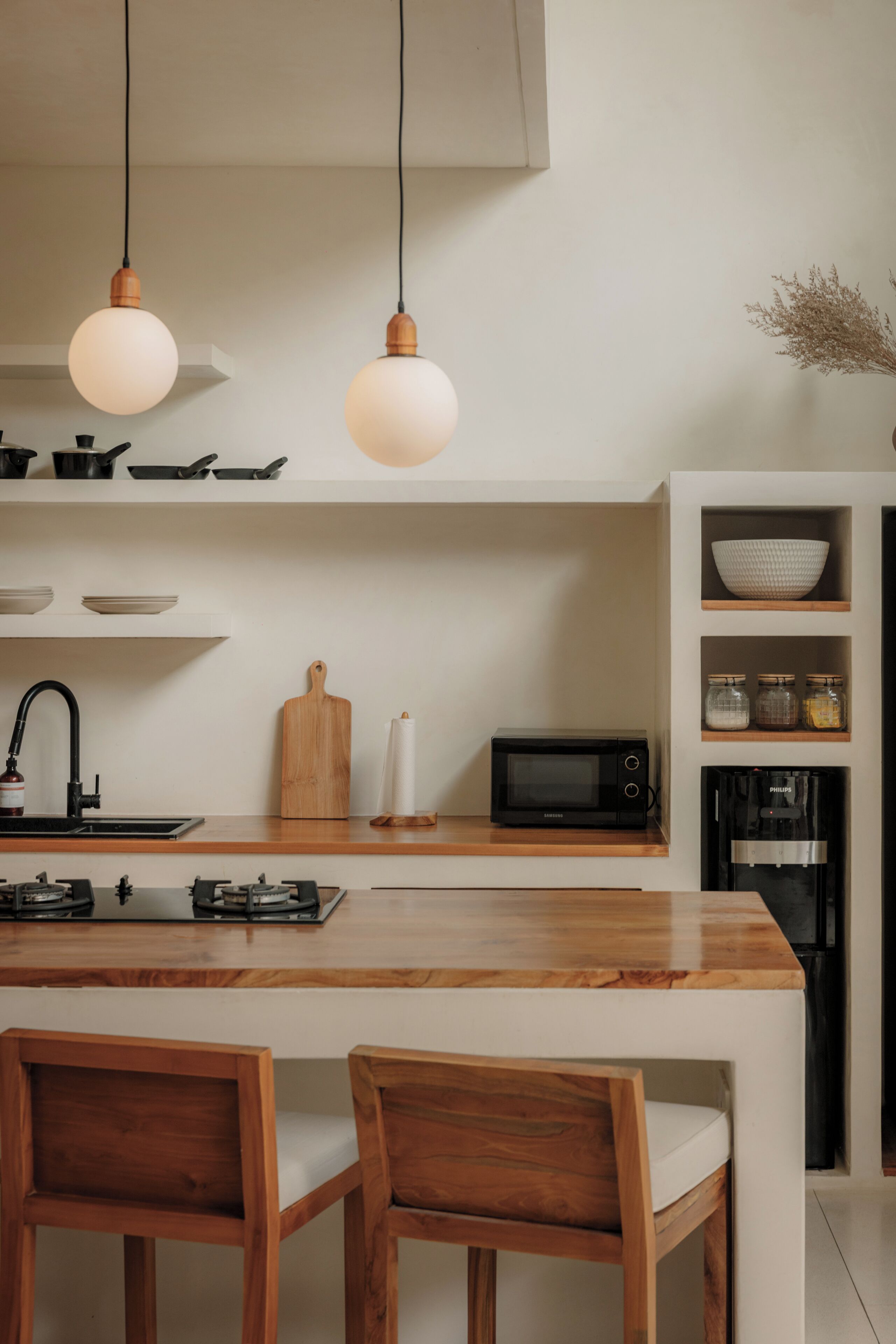 Una cocina con una isla de madera, dos lámparas colgantes, un microondas, una cafetera y un fregadero.