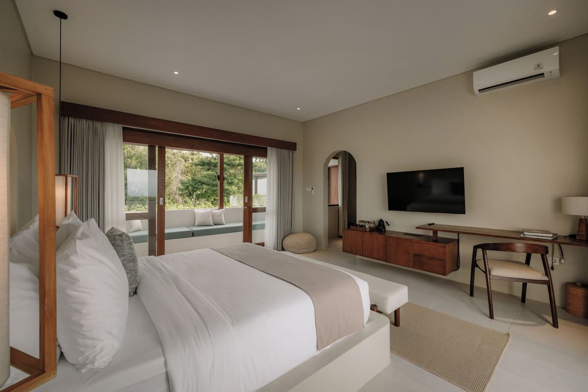 Une chambre moderne avec un grand lit, une télévision, un bureau et une vue sur la verdure environnante.