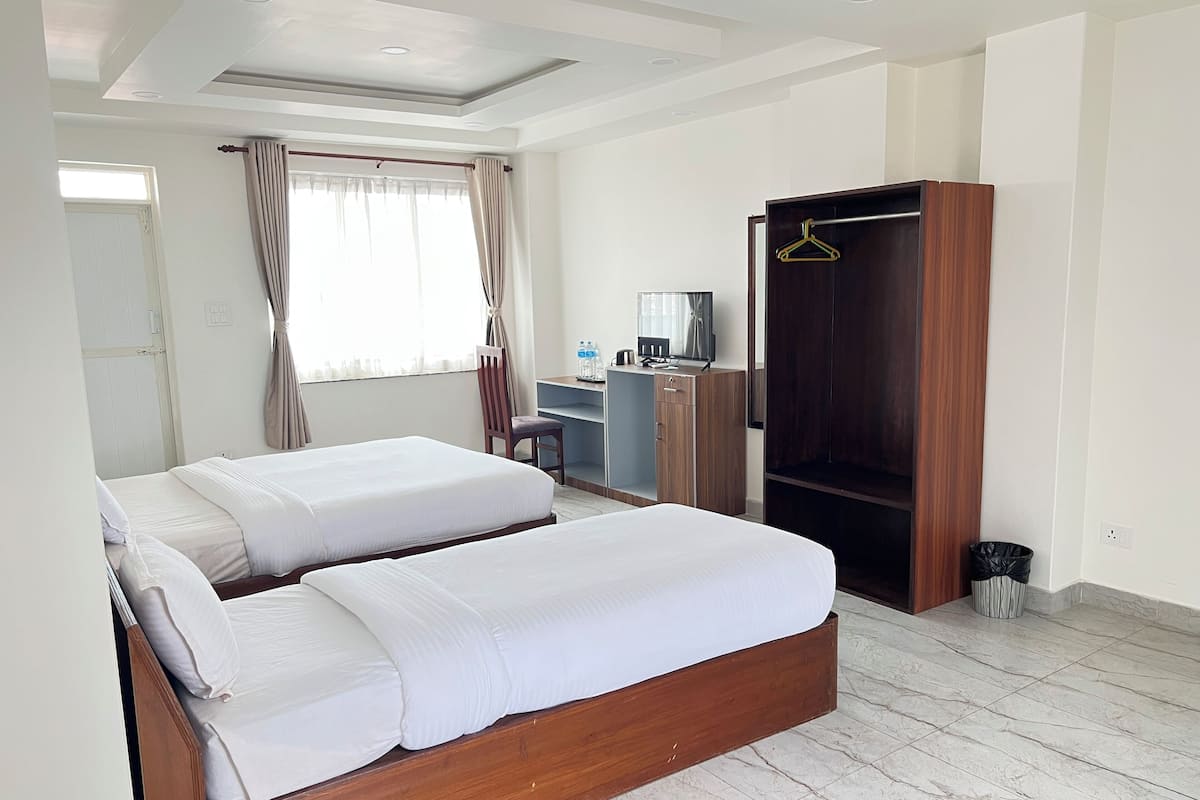 A hotel room with two beds, a desk, a wardrobe, and a window with curtains.