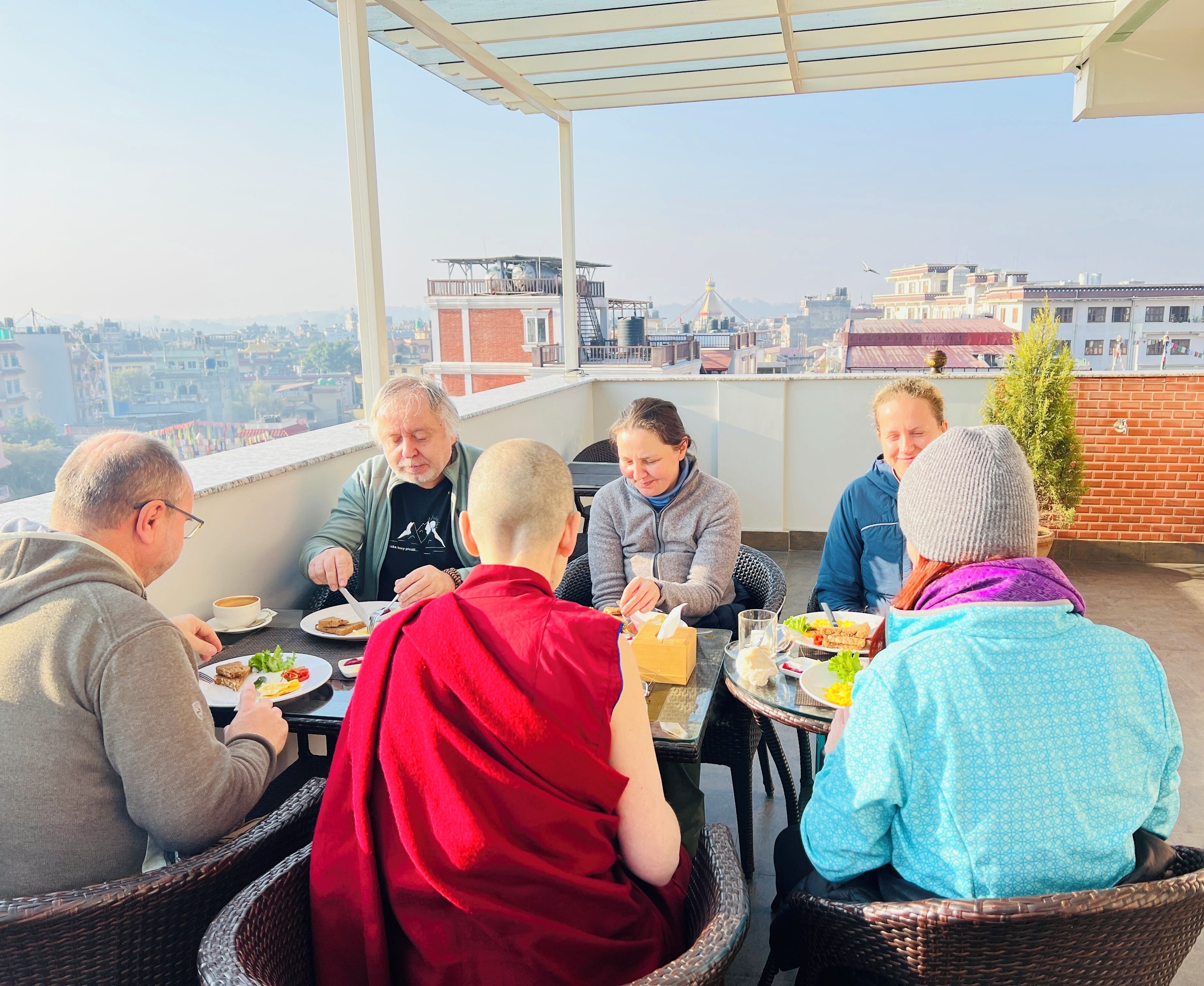 Um grupo de pessoas jantando ao ar livre em um terraço, com vista para a cidade.