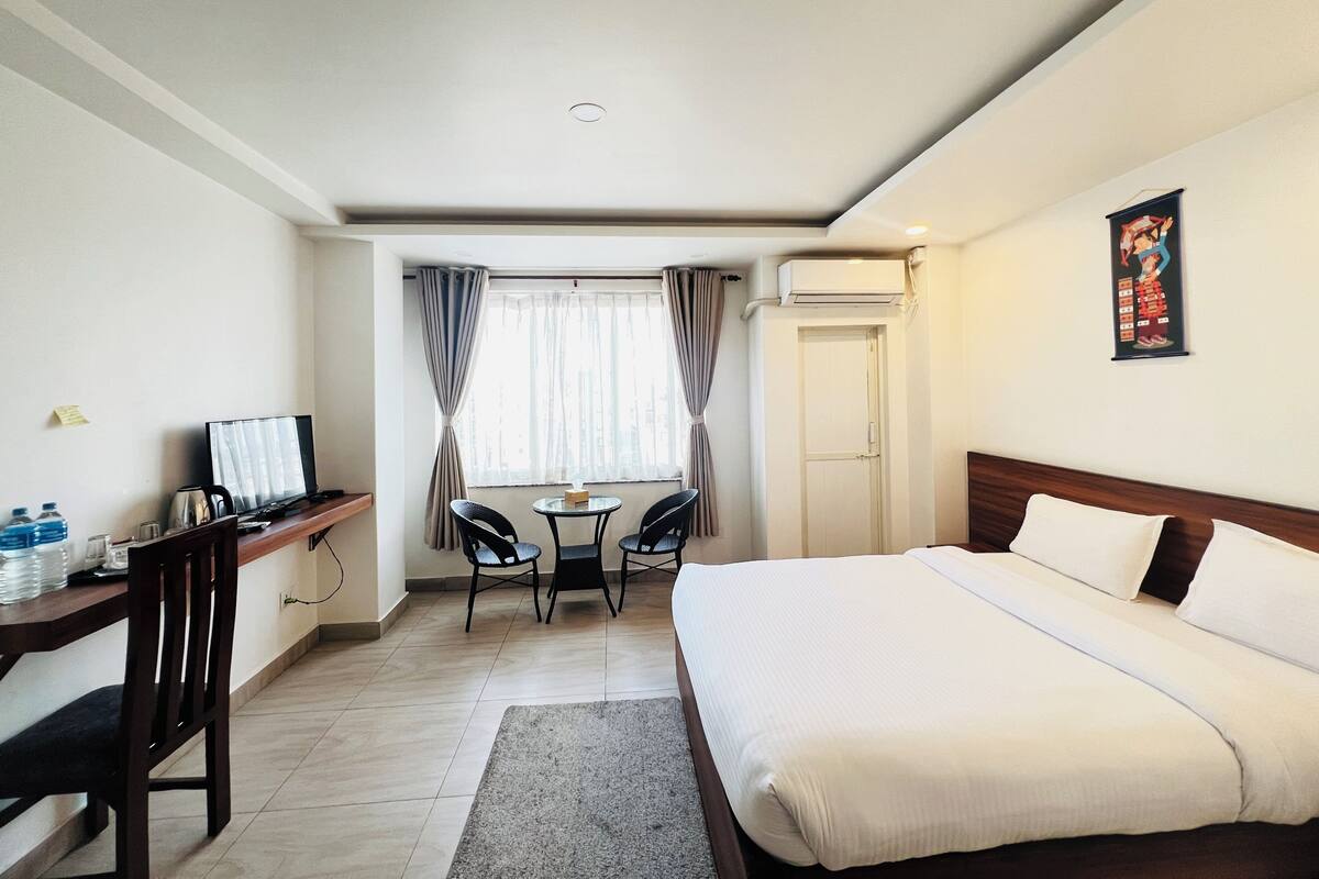 A hotel room with a bed, desk, chair, and a small table with a chair.