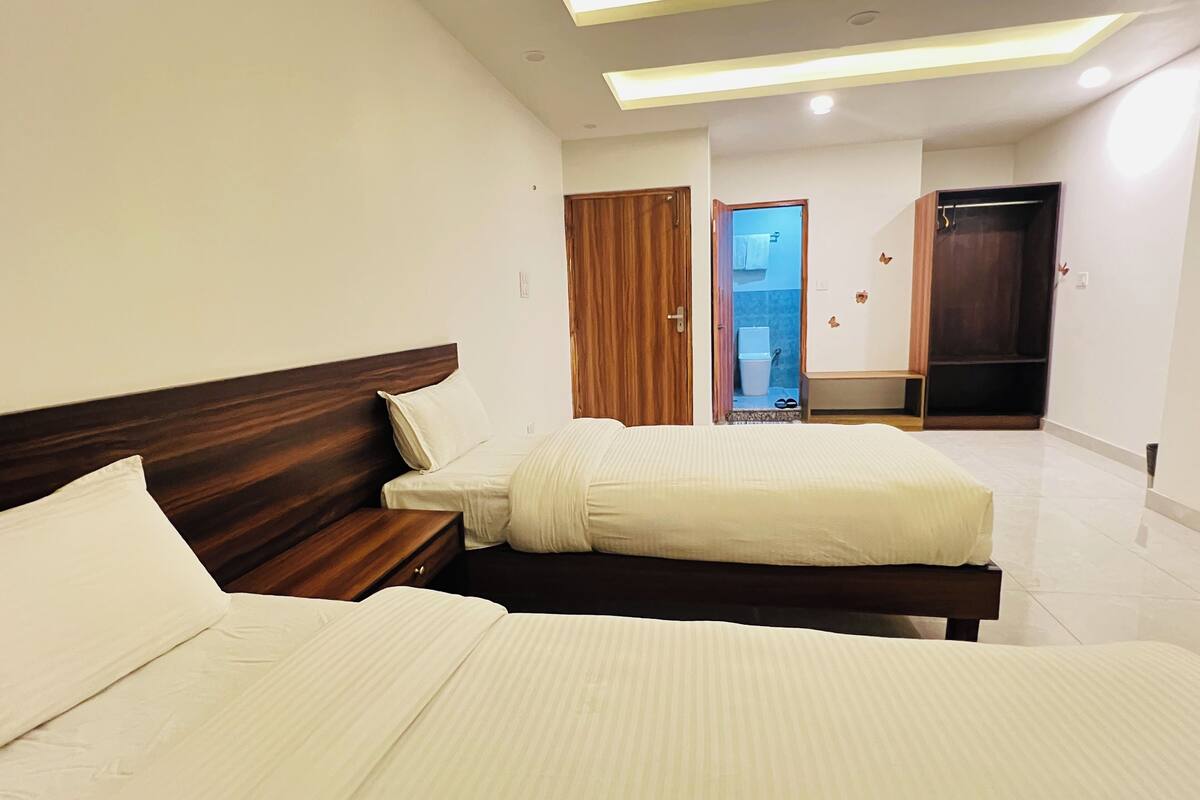 A modern hotel room with two beds, a wooden headboard, and a bathroom visible through an open door.