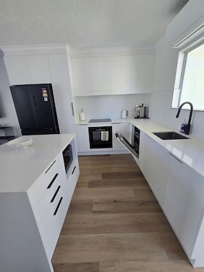 A modern kitchen with white cabinetry, a black refrigerator, and a wooden floor. - 2Br - Walk to Beach and Dining (North Ward)