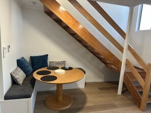 A modern interior with a round wooden table, a built-in bench with cushions, and a wooden staircase. - 2Br - Walk to Beach and Dining (North Ward)