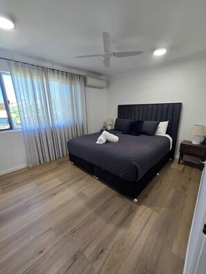 A modern bedroom with a large bed, a ceiling fan, and a window with curtains. - 2Br - Walk to Beach and Dining (North Ward)