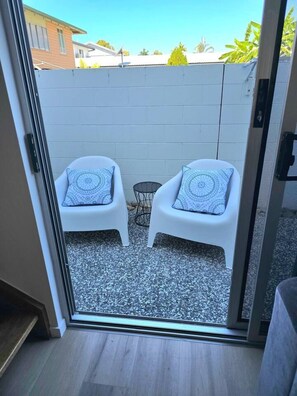 A sliding glass door leading to an outdoor patio with two white chairs and a small round table. - 2Br - Walk to Beach and Dining (North Ward)